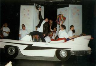 The cast of ''Summer Nights''in 1950s gear acting to the 'Greased Lightening' song in and around a pink and white Cadilac